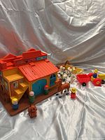 Vintage Fisher Price Little People Western Town building with figures and animals arranged around it on a gray backdrop.