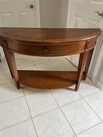 Photo showing the full vintage wooden hall table with curved front, drawer and bottom shelf from an angled view