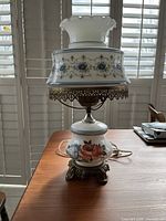 Full view of the vintage hurricane lamp showing the white glass top with scalloped edges, blue and white patterned midsection, metal trim, and floral painted base.