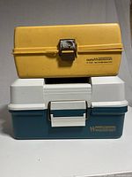 Two stacked closed tackle boxes; yellow Old Pal II Woodstream on top and green and white Woodstream box below.