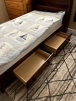 Wood twin captain bed partially assembled with mattress and quilt with sailboat design on top, drawer open showing interior
