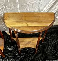 Photo of half-circle wooden demilune table with spindle legs and lower shelf on black fabric background
