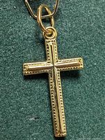 Close up photo of the gold cross pendant showing front detailing and bail loop on green fabric background