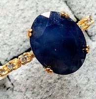 Close-up top view of deep blue oval sapphire and diamond-set textured gold shoulders