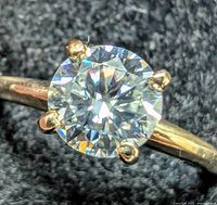 Close-up top view of the round brilliant moissanite in six-prong yellow gold setting against dark background