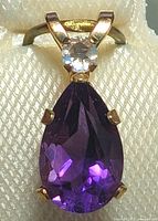 Close-up front view of the pendant showing the pear-shaped purple amethyst and small white stone at the top with yellow gold settings.