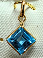 Close-up of pendant showing square blue topaz in yellow gold setting attached to bail.