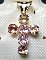 Close-up of the pendant showing the six round faceted tourmaline stones in pink, purple, and peach hues arranged in a cross shape with 10K yellow gold prong settings and a polished gold bail.