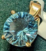 Close-up of round blue topaz set in four-prong 14K yellow gold on green background