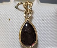 Close-up photo of 14K gold ammolite pendant focused on front face of stone and bail, showing teardrop shaped dark ammolite gemstone with gold decorative setting.