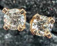 Close-up front view of two 14K yellow gold stud earrings each with a round lab diamond in 4-prong settings.
