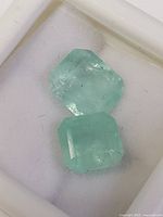 Two light green Columbian emerald loose gemstones placed inside a white display box, showing cut and clarity