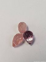 Three faceted gemstones arranged together, two pink and one purple teardrop-shaped.