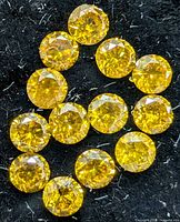 Close-up view of 14 round yellow diamonds on black fabric showing facets and color.