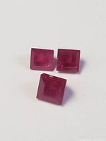 Photo showing three square-cut rubies from a top view, highlighting color and cut details.