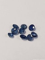 Nine loose blue sapphire gemstones on a white background, showing top view with faceted cuts.