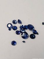 Loose blue sapphires displaying multiple cuts and shades of deep blue color scattered on a plain white background.