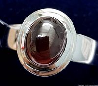 Close-up photo of silver ring featuring a smooth oval garnet stone set in a bezel setting.