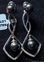 Photo of silver earrings with black pearl and cubic zirconia stones on a black background.