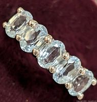 Close-up of silver ring with oval blue topaz gemstones showing detail of stones and prongs.