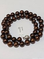 Full view of the silver dyed dark brown freshwater pearl necklace laid in a coiled manner showing pearl size and overall condition.