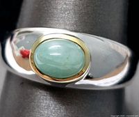 Close-up of ring showing oval emerald gemstone set in gold bezel on polished sterling silver band.