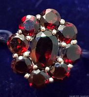 Close-up image of silver garnet ring showing oval center stone surrounded by smaller round garnet stones in a cluster setting.