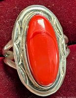 Close-up front view of the silver ring showing the bright red elongated oval gemstone with engraved silver bezel and split shank band on a red backing.