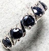 Close-up image of silver ring with five round blue sapphires in prong settings and twisted silver design between stones.