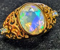 Close-up front angle showing oval faceted natural opal with vibrant play of color in a detailed openwork band with two accent stones.