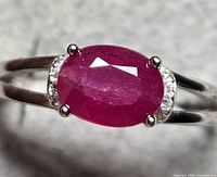 Close-up photo of silver ring showing the oval ruby and small clear accent stones on the band.