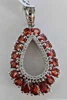 Close-up front view of the teardrop-shaped silver pendant with red gemstones and clear accent stones