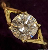 Close-up of round brilliant cut yellow moissanite set in prongs on silver yellow-toned geometric designed band.