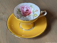Front and top view of Aynsley tea cup with pink rose design inside and yellow saucer
