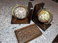 Pair of globe bookends with vintage map globes on wooden bases and carved wooden book-shaped box in foreground.