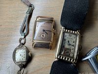 Close-up photo of three vintage wristwatches including two Bulova brands with rectangular faces and one non-specified watch with ribbed bezel and leather strap.