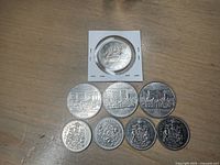 Coins laid out on a wooden surface showing reverse sides with Canadian maritime themes and coat of arms on smaller half dollar coins.