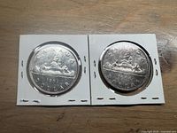 Front sides of 1953 and 1959 Canadian silver dollars showing the canoe with two voyageurs and tree.
