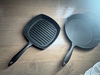Photo showing the 10-inch square ridged cast iron griddle and 12-inch round skillet with handles side by side on wooden surface.