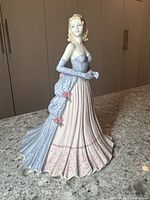 Full side and front view of the porcelain Coalport figurine showing hairstyle, gown, and glove details.