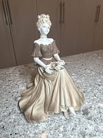 Front view of Coalport figurine showing elegant seated woman in detailed gown on granite surface