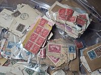 View of multiple early Canadian postage stamps attached to various paper scraps and envelopes in plastic bags, showing a range of red, green, and blue stamps mostly from the 1920s-1930s era.