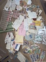 Top-down photo showing large assortment of early Canadian stamps and envelopes scattered on floor, includes used stamps, unused sheets, and stamps on envelopes.