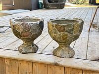 Front view of both concrete and rock planters on wooden deck showing exterior rock inlay and pedestal base.