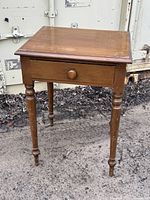 Front and angled front photos showing overall shape, drawer, and tapered turned legs of antique side table.