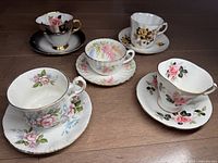 Top view of the five English bone china cups and saucers arranged on wooden surface showing floral patterns and shapes.