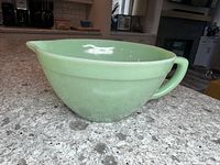 Side view of the green FireKing Jadeite batter bowl showing the pouring spout and handle, placed on a gray speckled countertop.