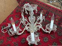 Full view of five arm glass chandelier laid on red patterned rug showing clear glass arms, candle-shaped bulbs, and glass prisms.