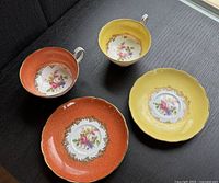 Two Grosvenor cups and saucers, one orange set and one yellow set, showing floral painted interiors and gold gilding.