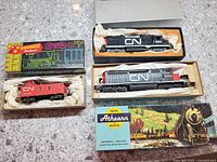 Tenshodo GP-35 Diesel engine in original silver box beside other CN train cars and packaging on counter.